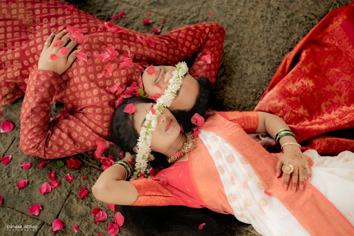 Couple lying head to head among rose petals, a jasmine garland in her hair