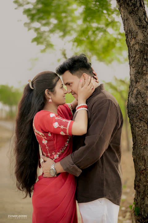 Couple embracing forehead to forehead beside a tree trunk